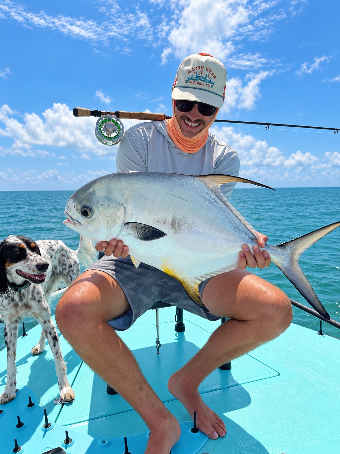 Pierce August holding a permit he caught, with his dog on the bow of the flats boat