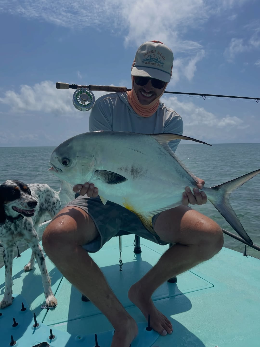 Pierce August holding a permit on the bow of a flats boat with his dog